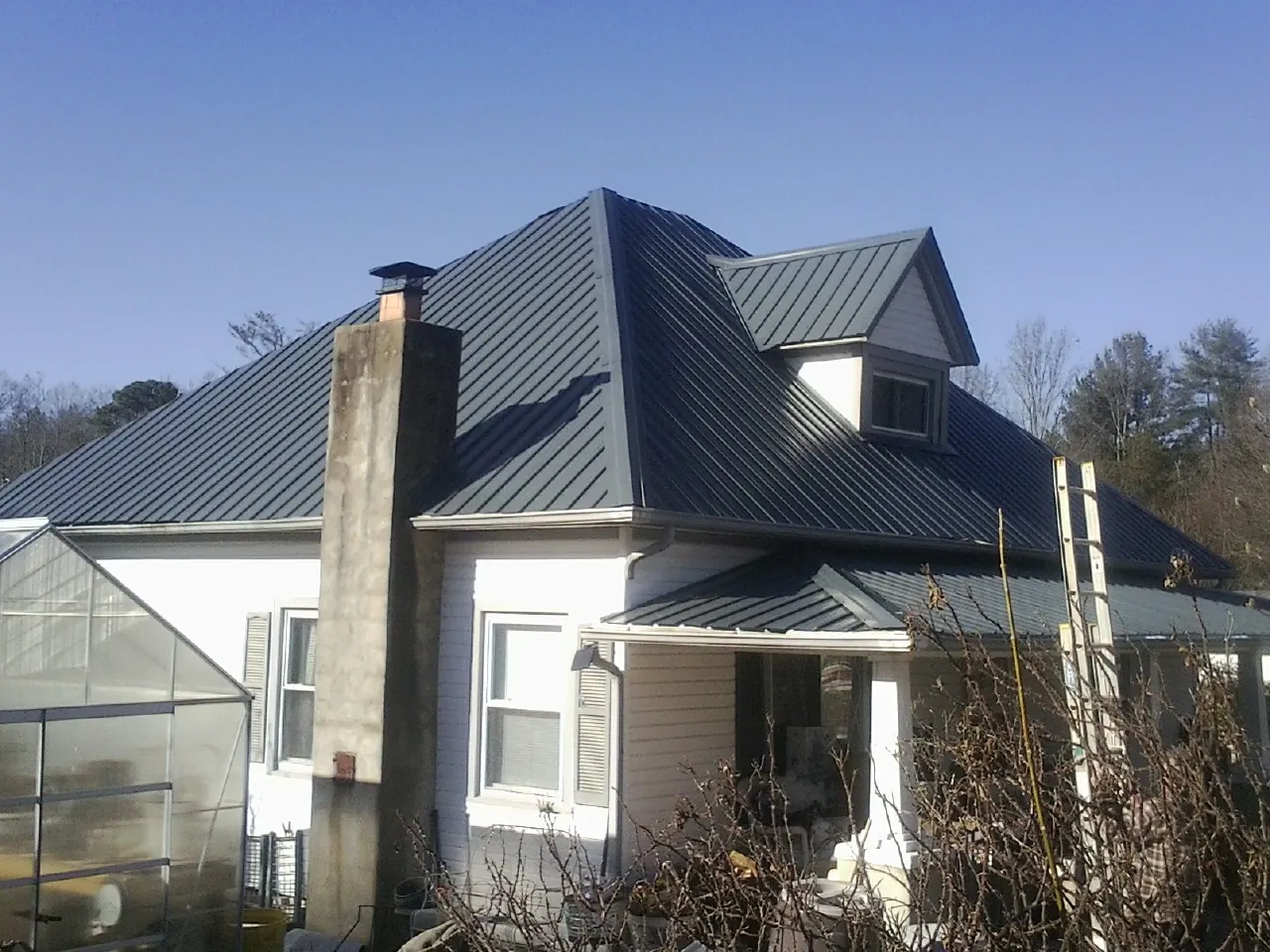 Dark blue standing seam metal roof on a white farmhouse with dormer — Slate & Tile Roof Repair by Roofing Brothers in Eldorado