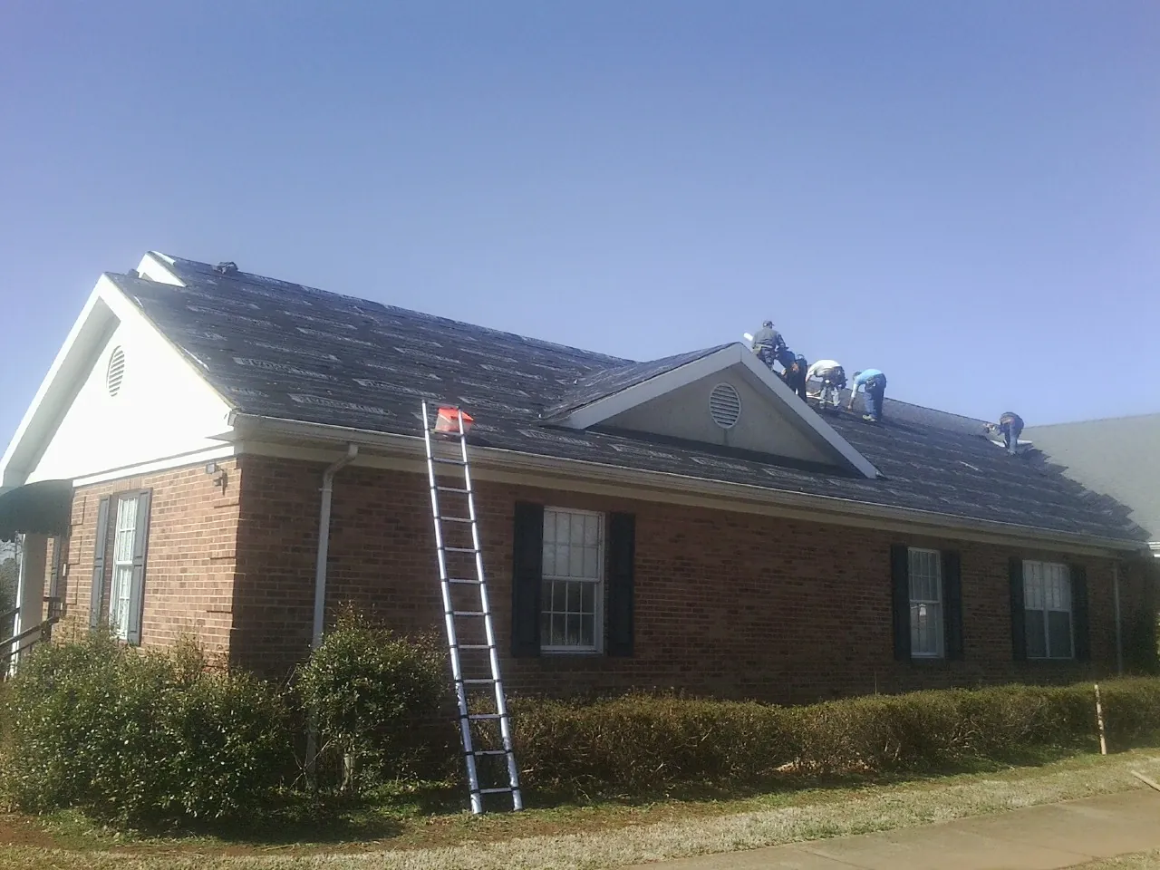 Crew tearing shingles off a brick ranch roof with a ladder set — Emergency Roof Repair work by our crew in Eldorado