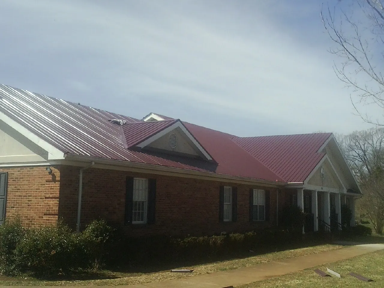 Red metal roof with gabled entries on a long brick building, from a Hail Damage Roof Repair job in Eldorado