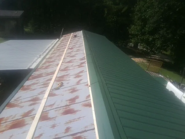 Old rusted panels beside newly installed green metal roofing — Wind Damage Roof Repair by Roofing Brothers in Eldorado