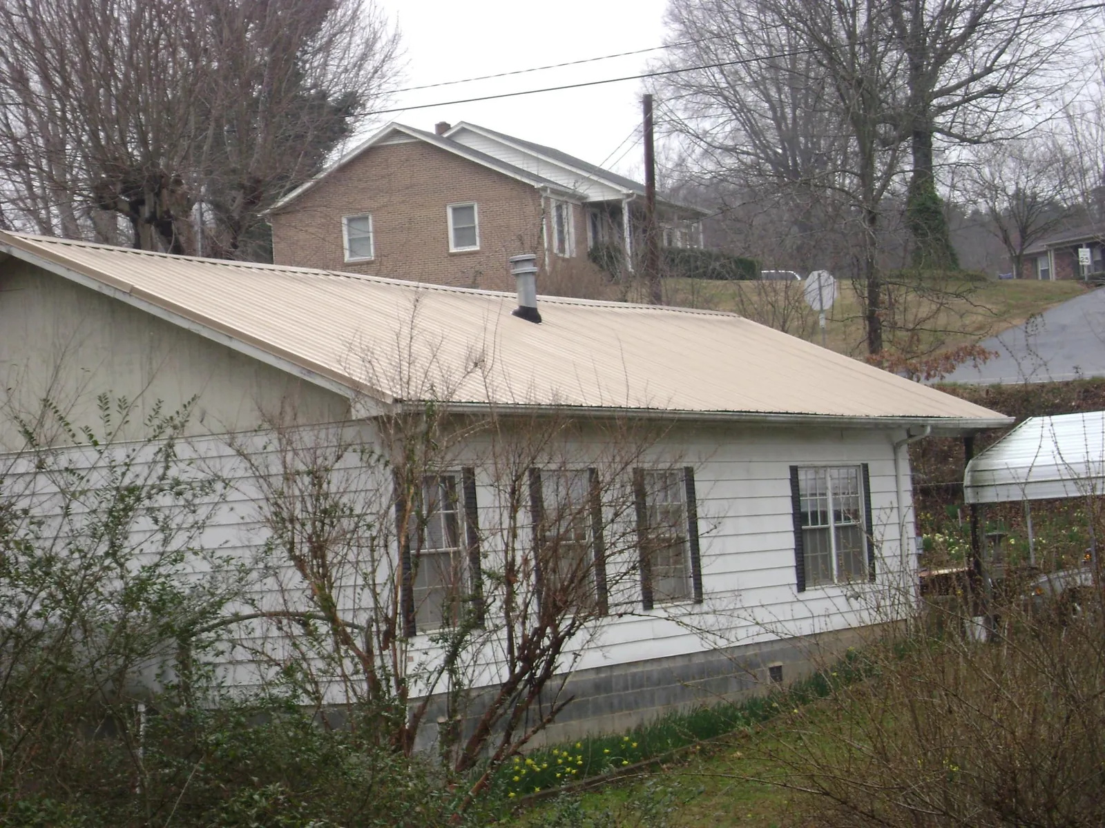 Tan metal roof on a white sided house set into a hillside — Commercial Roofing by Roofing Brothers in Eldorado